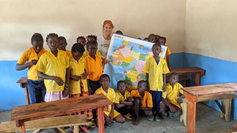 Profesora voluntaria de Yirewa rodeada de sus alumnos sosteniendo un mapa político de África